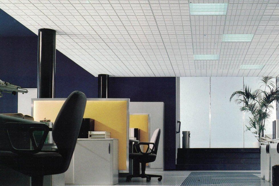 Moderno spazio di lavoro per ufficio caratterizzato da divisori per cubicoli gialli, controsoffitto a griglia e pareti di accento nere.