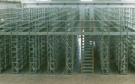 Un sistema di stoccaggio a più livelli per magazzini, con file di scaffalature metalliche grigie e una scala centrale in metallo.
