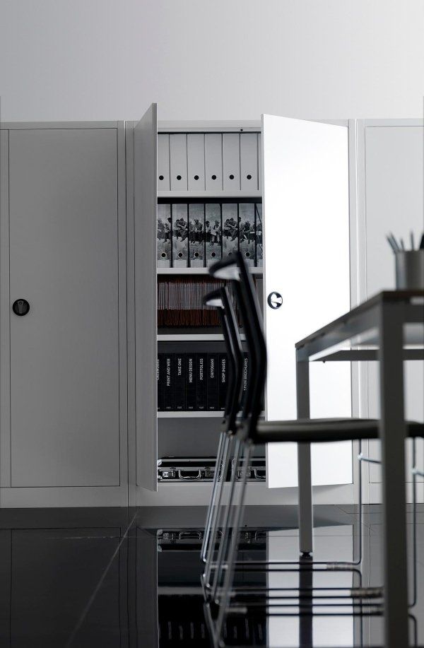 Un ufficio minimalista con un armadio bianco contenente raccoglitori ben organizzati, accanto a sedie e un tavolo su un pavimento lucido.