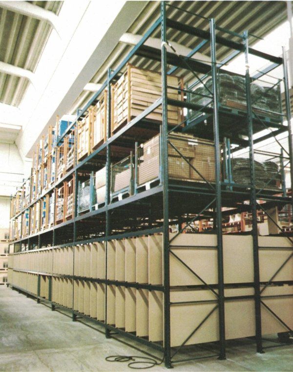 Scaffalatura industriale alta, tipica di un magazzino, che contiene casse di legno e pannelli piatti, vista da un'angolazione diversa all'interno di un deposito.