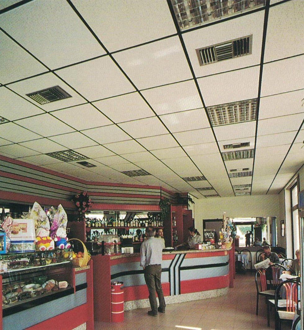 Un cliente è in piedi davanti a un bancone rosso, grigio e nero in una caffetteria caratterizzata da un soffitto a griglia con lampade integrate.