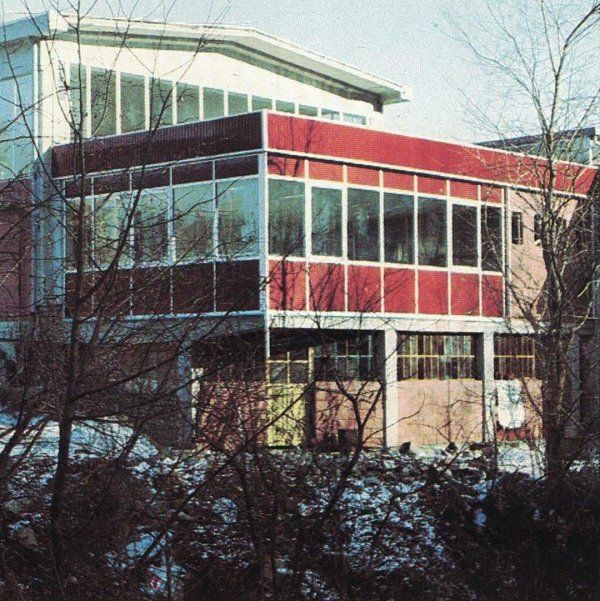 Un edificio a due piani con il piano superiore rivestito in pannelli rossi e finestre di vetro, visibile attraverso i rami spogli degli alberi in inverno.
