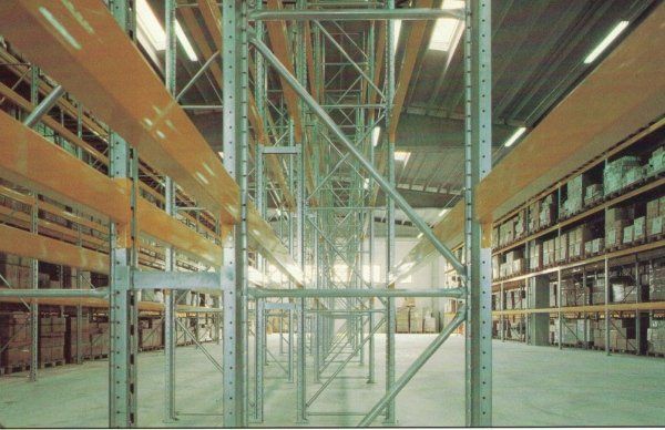 All'interno di un grande stabilimento industriale, file di scaffalature metalliche con ripiani arancioni e pavimento in cemento.