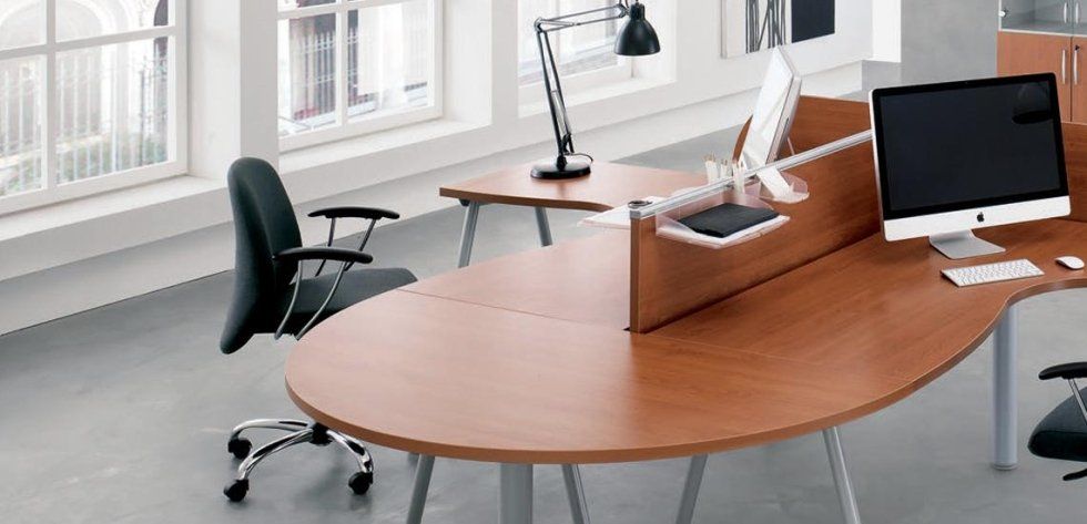 Moderno spazio di lavoro in ufficio con scrivanie in legno curve, sedie ergonomiche, un computer e lampade da scrivania in una stanza luminosa.