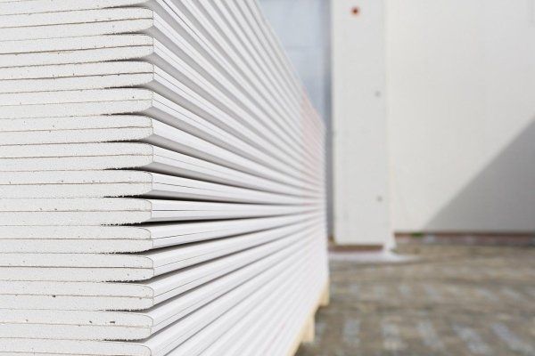 Una pila di pannelli di cartongesso bianco per pareti, riposti su un pallet di legno all'aperto.