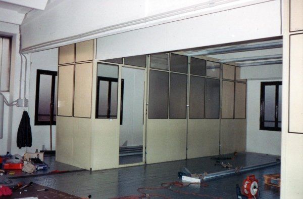 Vista interna che mostra la ristrutturazione di un ufficio con l'installazione di una nuova parete divisoria modulare in vetro e laminato.