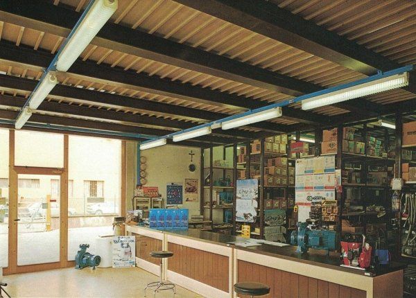 Un bancone di servizio in un negozio con pannelli marroni, scaffali pieni di provviste e luci fluorescenti su un soffitto a doghe.