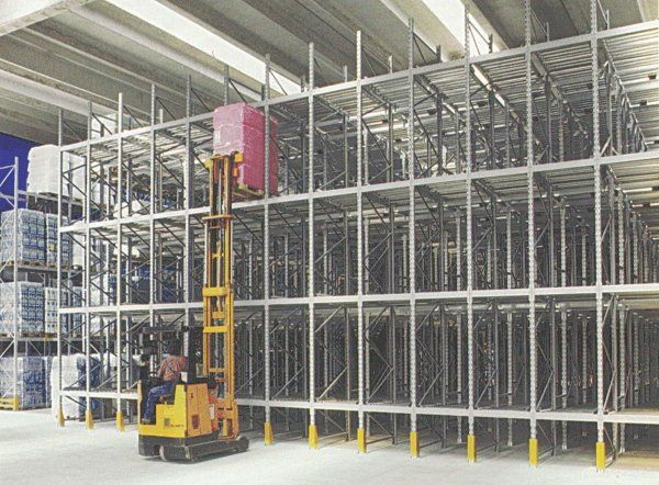 Un operatore di carrello elevatore solleva un pallet rosa acceso su una scaffalatura metallica a più livelli all'interno di un magazzino.
