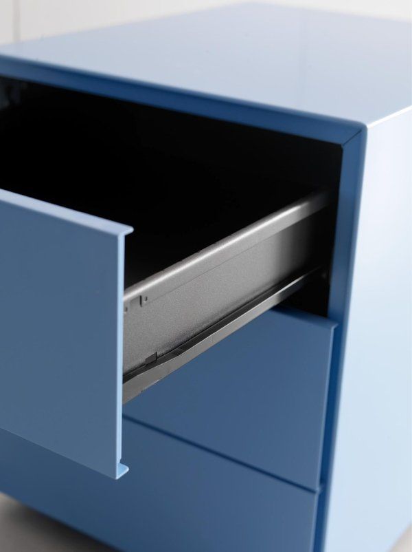 Un comodino lucido di colore azzurro chiaro con un cassetto superiore parzialmente aperto che rivela una guida metallica e un interno scuro.
