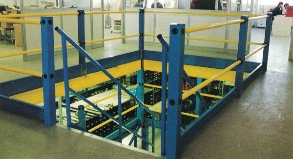Scala e ringhiera industriali blu e gialle che circondano un'apertura nel soppalco.
