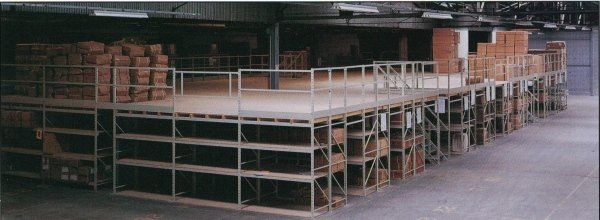 Un sistema di scaffalature a soppalco industriale a più livelli all'interno di un magazzino, pieno di scatole e casse impilate.