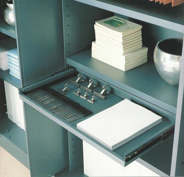 Una scaffalatura in metallo color verde acqua con un cassetto estraibile a giorno contenente articoli per ufficio, libri e un vaso metallico.