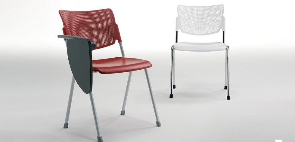 Una sedia da aula rossa con un bracciolo porta-tablet incorporato, accanto a una sedia bianca su uno sfondo chiaro e uniforme.