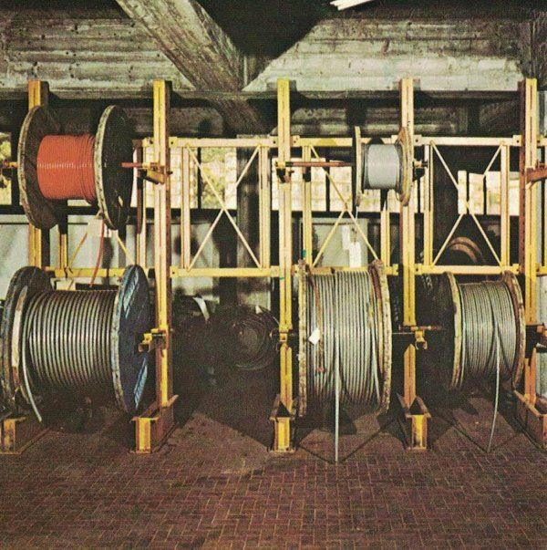 Grandi scaffalature metalliche industriali che contengono diverse bobine di filo e cavo di grosso spessore in un ambiente di magazzino.