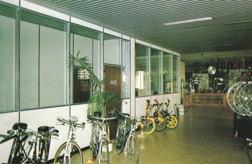 Una fila di biciclette parcheggiate in uno spazio interno luminoso e moderno con pareti a pannelli di vetro e un soffitto decorato.
