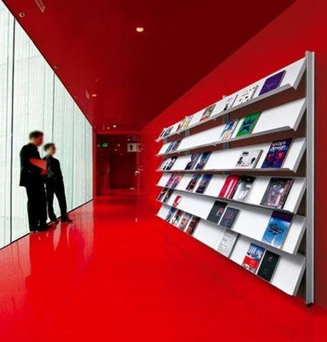 Due persone sono in piedi in un corridoio rosso acceso, accanto a una scaffalatura a muro su cui sono esposte file di riviste e libri.