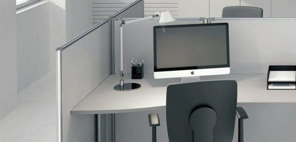 Una postazione di lavoro in ufficio con lampada da scrivania, monitor Apple, sedia da ufficio e vassoio portadocumenti.