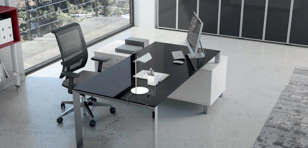 Una moderna scrivania da ufficio con piano in vetro nero, sedia e base bianche, situata in uno spazio di lavoro minimalista.