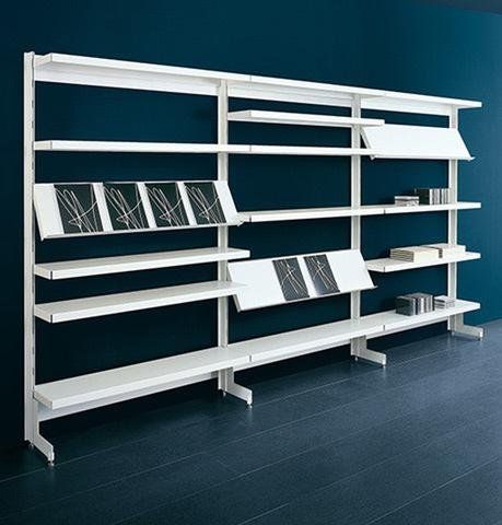 Una moderna libreria modulare a parete di colore bianco, con ripiani inclinati a vista, su uno sfondo blu scuro.