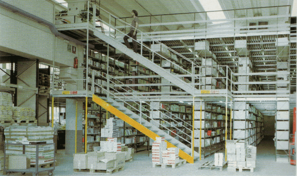 Un sistema di scaffalature industriali a più livelli con scala all'interno di un magazzino, con una persona che cammina sul livello superiore.