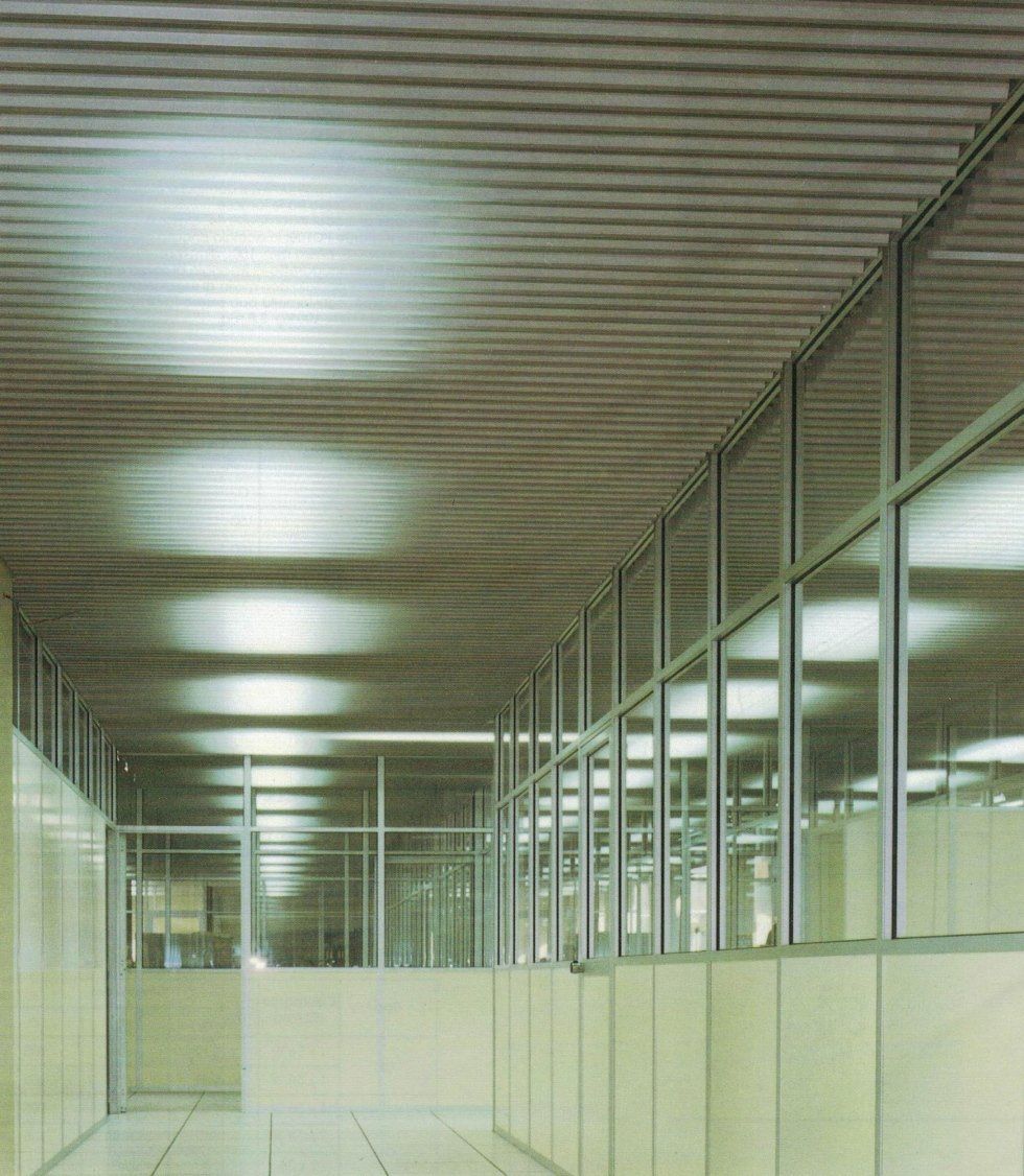 Vista prospettica di un lungo corridoio con pareti rivestite in vetro, pavimento chiaro e soffitto ondulato.