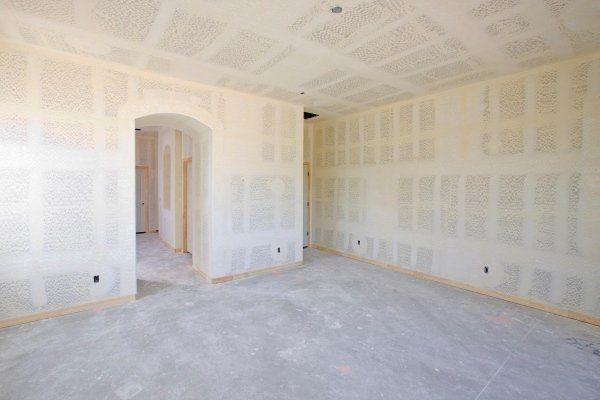 Una stanza non rifinita con pannelli di cartongesso beige, giunture stuccate e una porta che conduce a un altro corridoio.