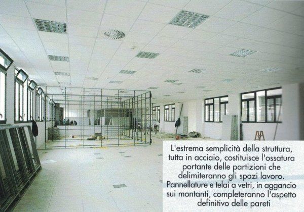 Interno di un ufficio in costruzione, che mostra la struttura metallica destinata alla futura suddivisione degli spazi di lavoro, con una didascalia esplicativa.
