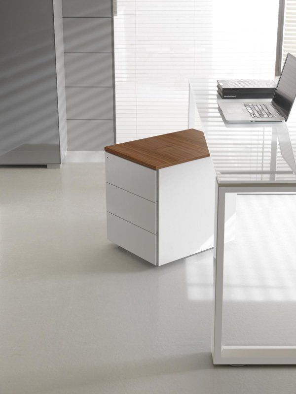 In una stanza moderna, uno sgabello da ufficio bianco con tre cassetti e piano effetto legno è posizionato su un pavimento chiaro vicino a una scrivania in vetro.