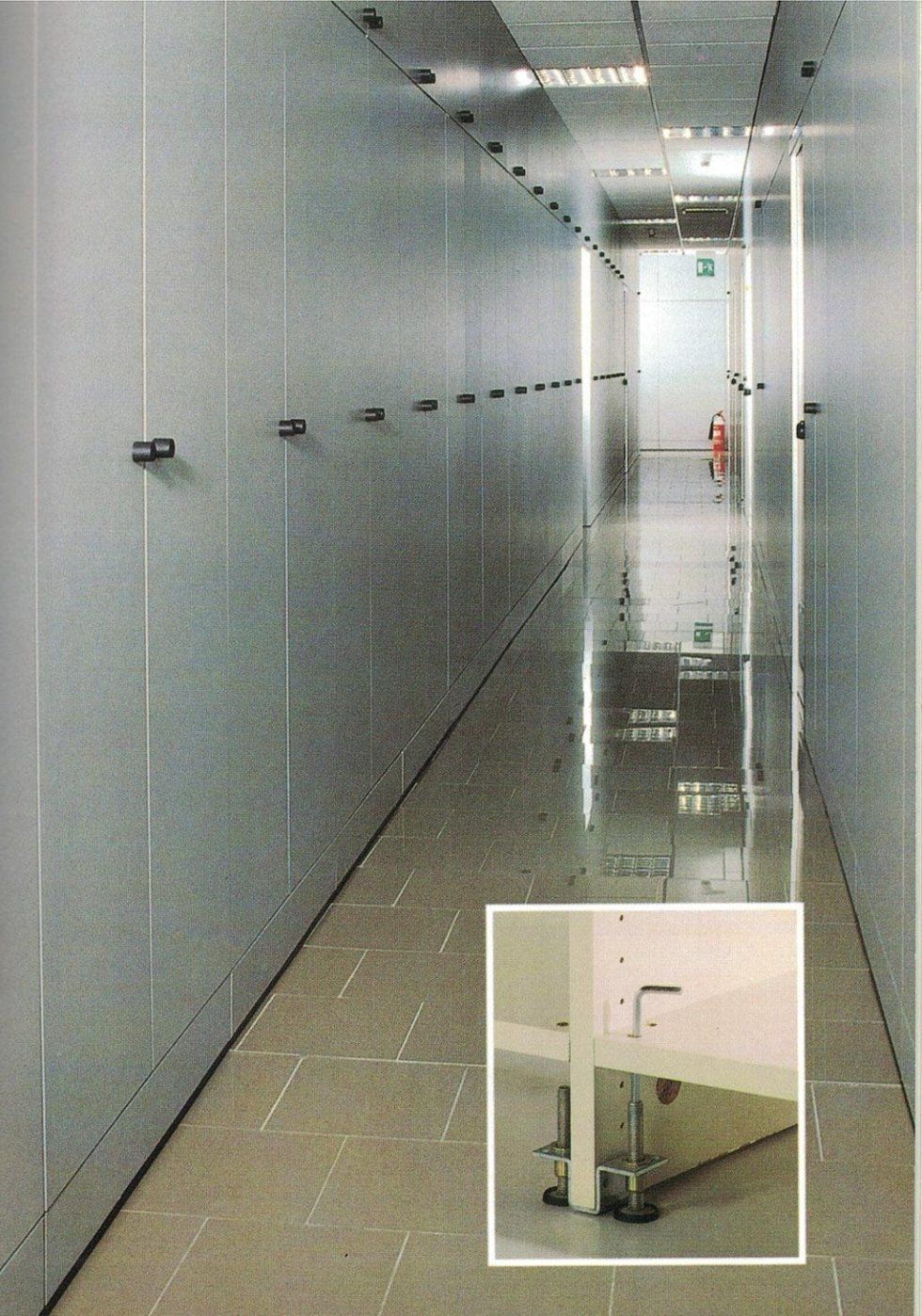 Uno stretto corridoio tra file di alti armadi grigi, con un riquadro che mostra i piedini di livellamento in metallo di un'unità .