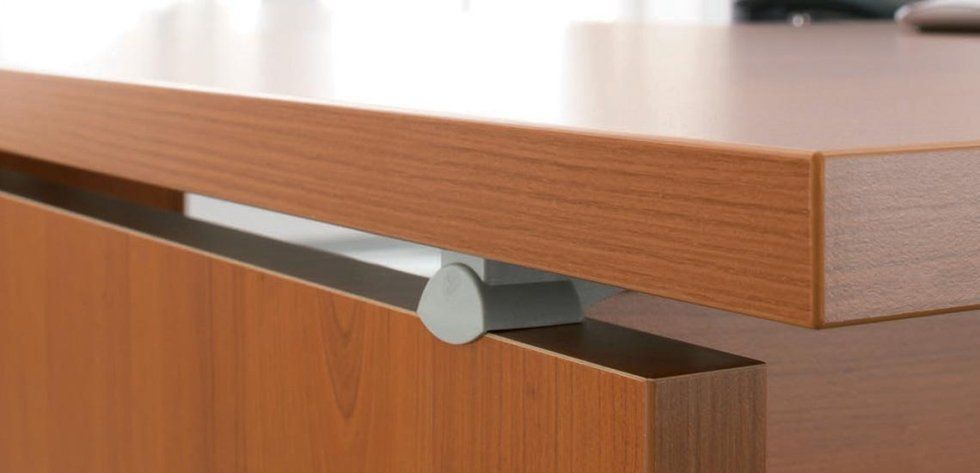 Primo piano di una scrivania in legno fissata a un pannello laterale tramite un elemento di fissaggio cilindrico in metallo argentato.