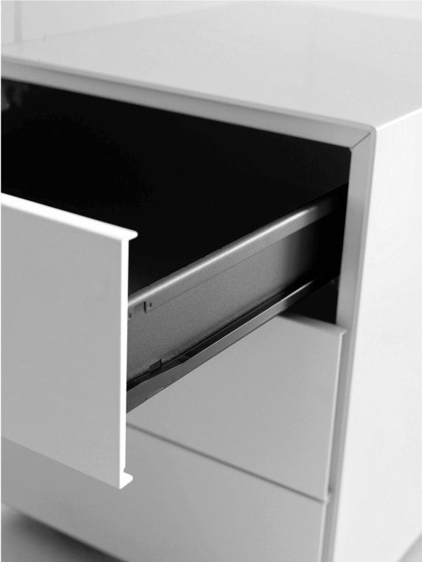 Un comodino bianco a tre cassetti, con il cassetto superiore aperto che rivela un interno scuro e guide metalliche.