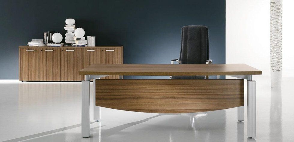 Una moderna scrivania direzionale in legno con pannello frontale curvo e mobile contenitore abbinato, su uno sfondo blu scuro.