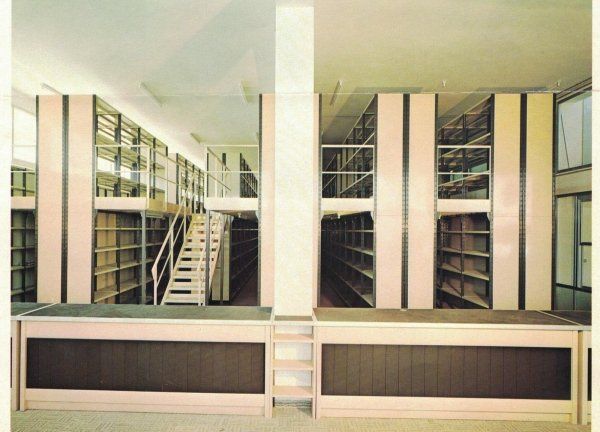 Scaffalature da biblioteca a due piani, nei toni del rosa pallido e del marrone scuro, con scala centrale e scrivania.