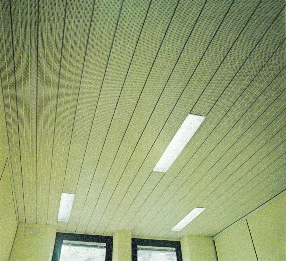 In una stanza, il soffitto è caratterizzato da listelli metallici lineari bianchi con pannelli luminosi rettangolari a incasso integrati.
