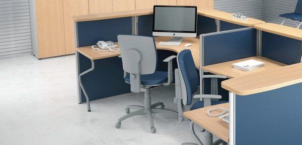Un gruppo di cubicoli per ufficio con scrivanie in legno chiaro, pannelli divisori blu scuro e sedie girevoli grigie.