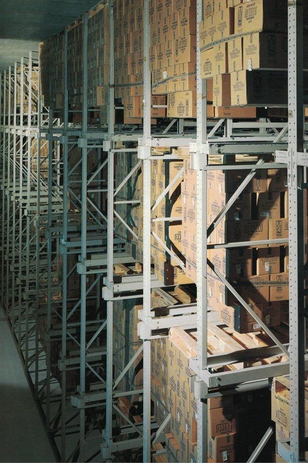 In un magazzino ad alta densità, file di scaffalature metalliche alte e di tipo industriale, piene di scatole di cartone.