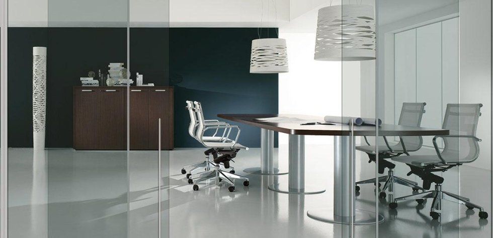 Una moderna sala riunioni d'ufficio con una parete scura, un mobile in legno, un tavolo con sedie in rete e lampade a sospensione decorative.