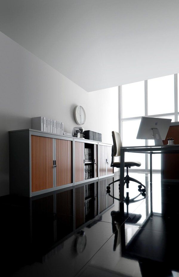 Un ufficio domestico minimalista con scrivania moderna, sedia e mobili contenitori in legno su un pavimento nero lucido.