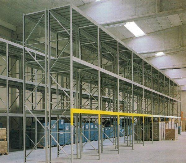 Una scaffalatura industriale in acciaio a più livelli all'interno di un magazzino, con una trave di sicurezza gialla al livello inferiore.