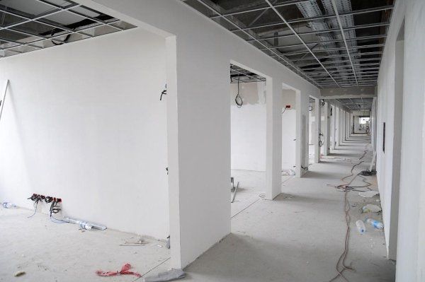 Un corridoio non rifinito con pareti bianche e travi metalliche a vista sul soffitto, durante un progetto di costruzione.