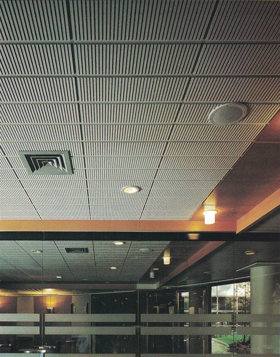Interni di ufficio moderni caratterizzati da un soffitto a griglia bianca perforata con illuminazione a incasso e bocchette di ventilazione.