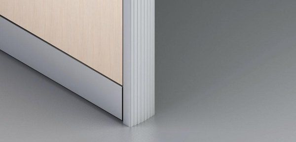 Una parete divisoria rivestita in legno chiaro con base color argento metallizzato e bordo laterale verticale a coste color argento, su un pavimento grigio.