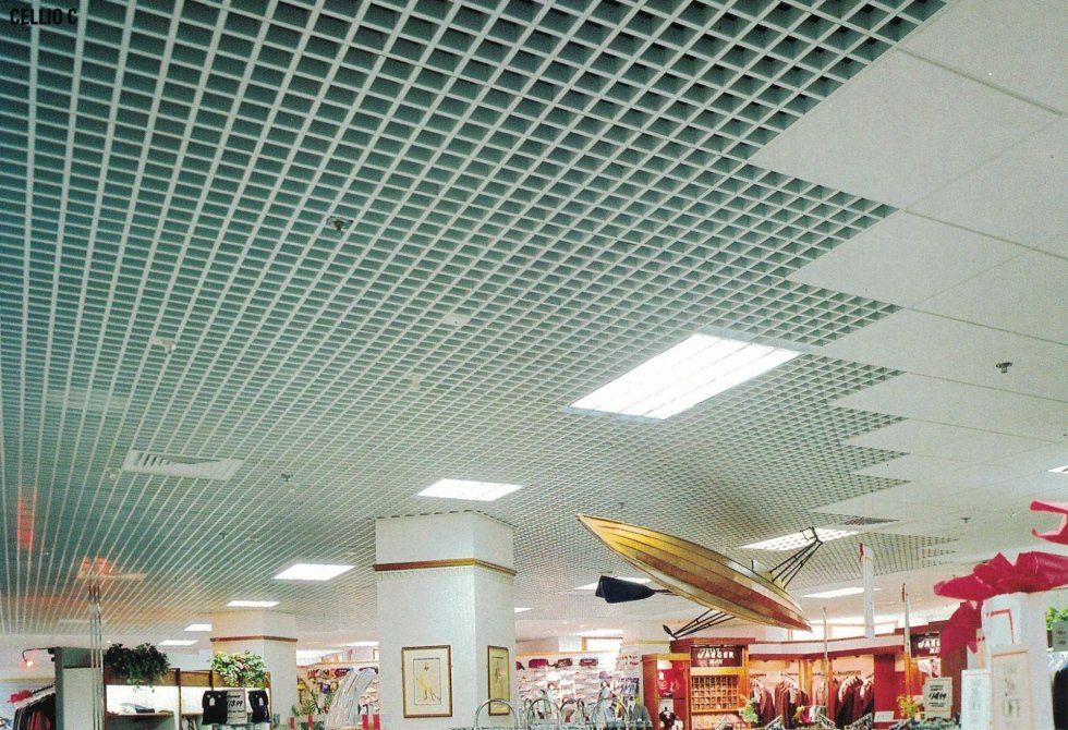 Un interno commerciale caratterizzato da un soffitto metallico a griglia aperta che si raccorda parzialmente a un controsoffitto bianco uniforme.
