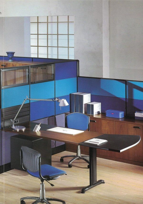 Un moderno cubicolo da ufficio con scrivania in legno, sedie da ufficio blu e pareti divisorie modulari sui toni del blu.