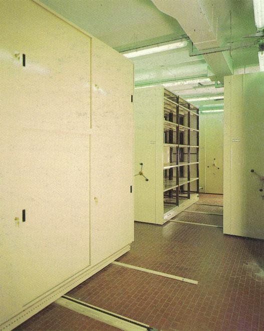 File di scaffalature mobili beige su binari in un luminoso e spazioso magazzino o archivio.