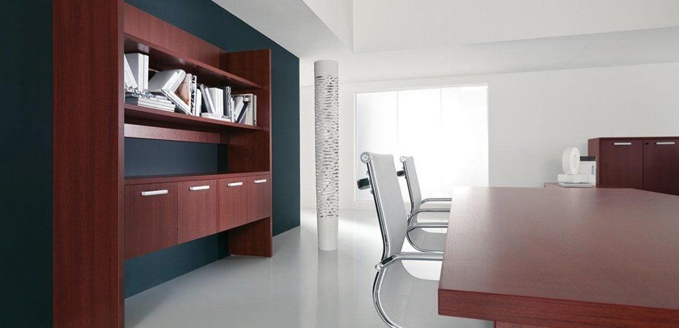Un ufficio moderno caratterizzato da un mobile in legno con librerie integrate, una parete scura a contrasto e sedie da conferenza disposte attorno a un tavolo.