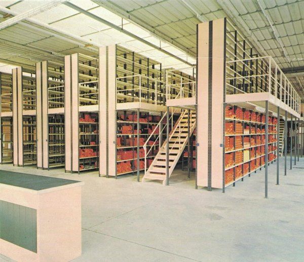 Sistema di scaffalature industriali a più livelli con scala, riempito di contenitori arancioni in un grande magazzino luminoso.