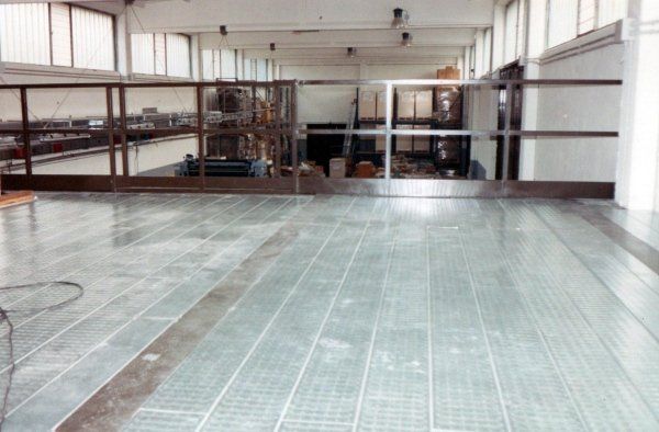 Pavimento sopraelevato in un magazzino industriale con superficie a griglia metallica e parapetto di sicurezza che si affaccia sul livello inferiore.