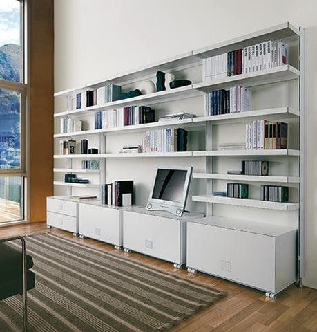 Un sistema di scaffalature a parete minimalista di colore bianco, che ospita libri, dispositivi elettronici e armadietti contenitori in un soggiorno moderno.