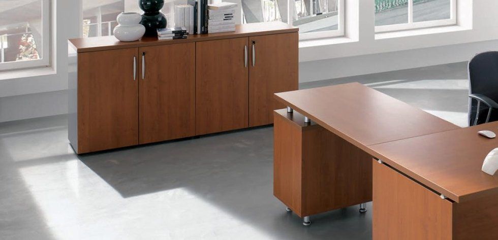Un ufficio moderno e luminoso, arredato con una scrivania in legno dotata di cassettiera su ruote e un armadio contenitore a quattro ante abbinato.